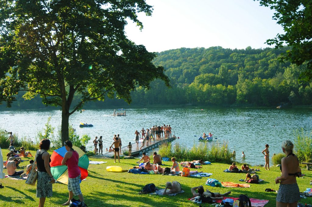 Groß und Klein tummeln sich an hießen Sommertagen am Badesee in Pfuhl unter schattigen BäumenAusflugsziel für Familien in Bayern